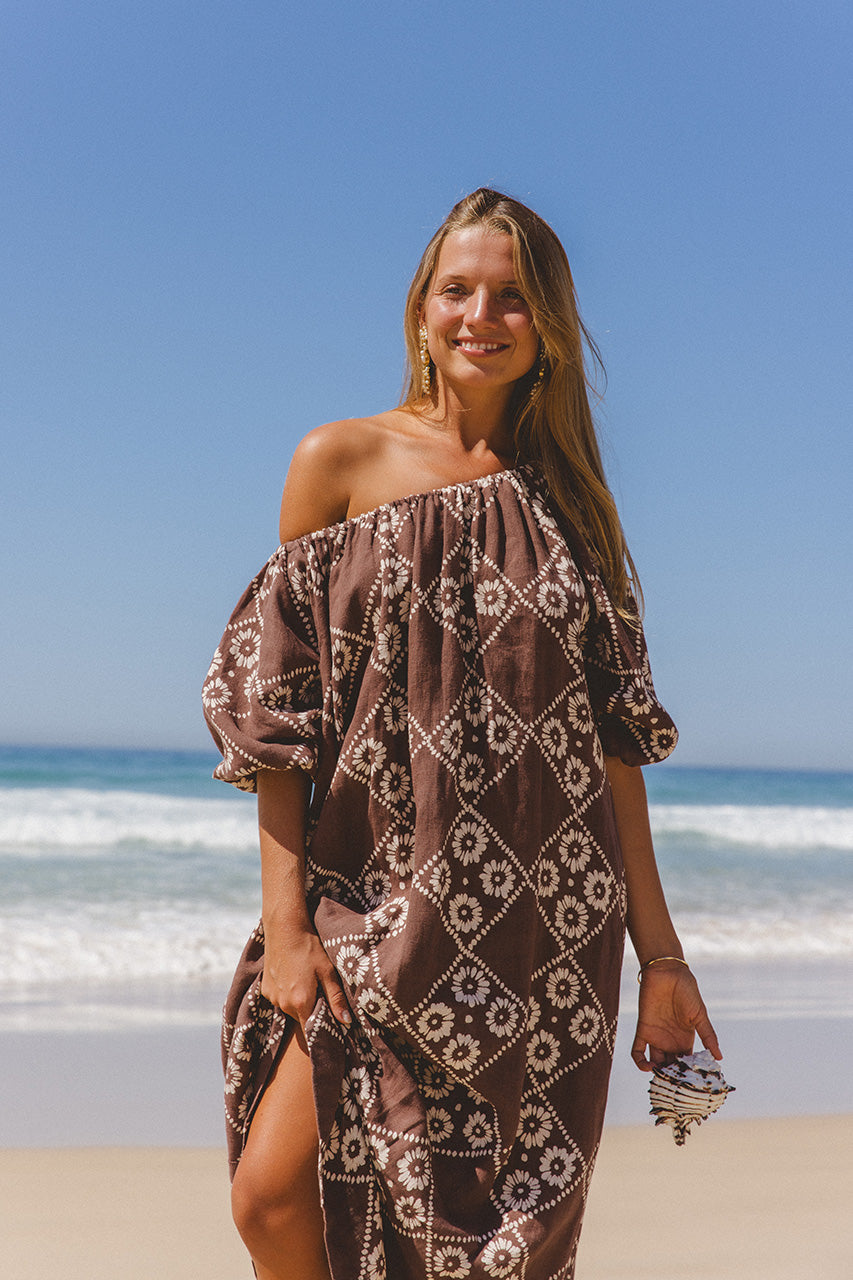 Dahlia Maxi Dress Maple — waist-up beach portrait, off-shoulder, smiling model holding shell, hand block print linen in maple brown | Daughters of India