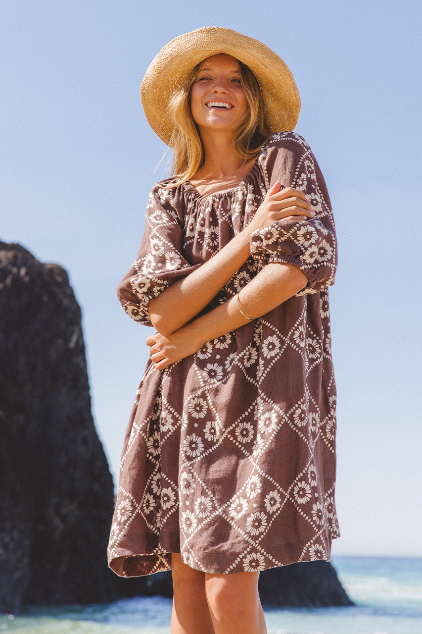 Dahlia Mini Dress Maple — smiling model at beach, front view full length, straw hat and maple brown hand block print linen mini, diamond daisy block print, boho ethical fashion | Daughters of India