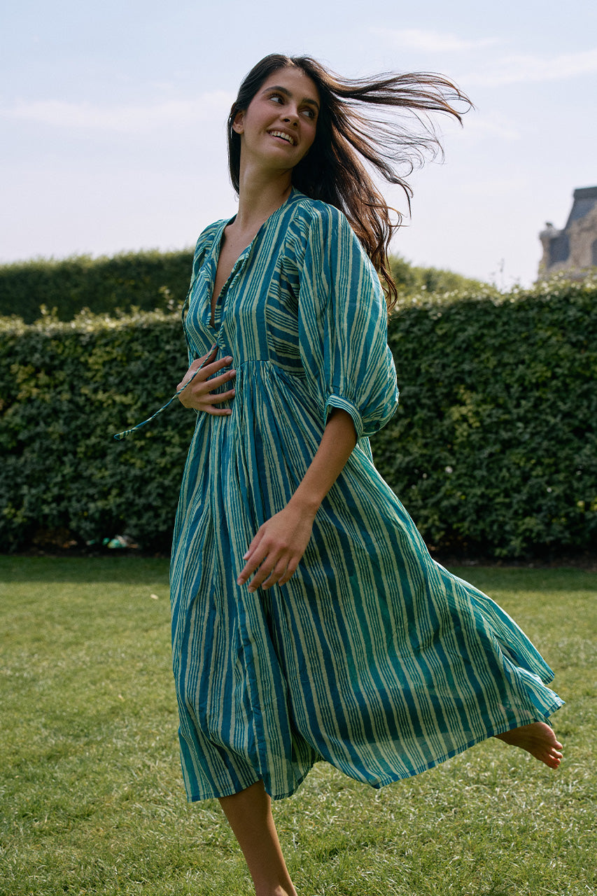 Woman spinning joyfully on grass wearing the Daughters of India Kyra Midi Dress in Spearmint, the flowing green striped dress swirling with hair in the wind