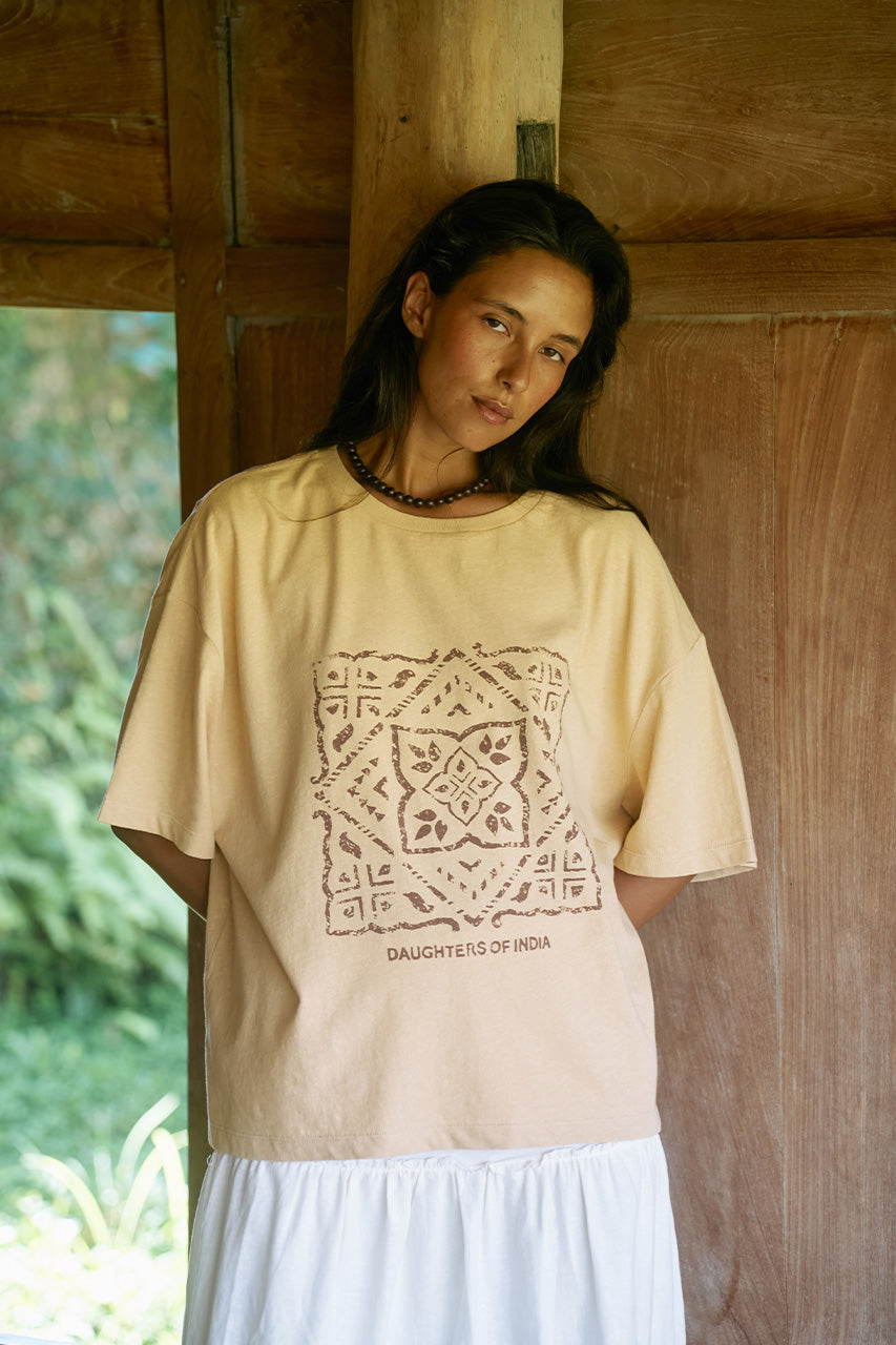 Woman wearing the Daughters of India Shanti Tee in Cashew, an oversized cream linen-cotton blend t-shirt with block print design, paired with a white skirt