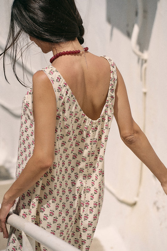 Back view of woman on white stairs wearing the Daughters of India Sundress Midi in Peony, showcasing the low open back and shoulder straps with a red beaded necklace