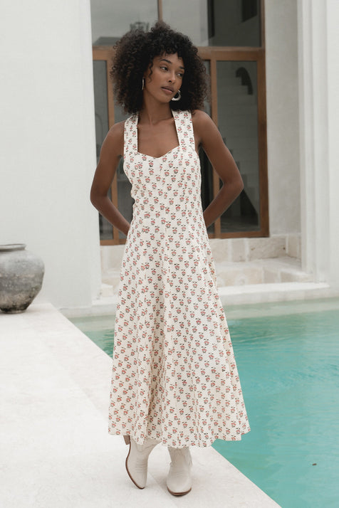 Lalika Dress Peony — full length front view by villa pool, peony hand block print cotton wrap dress with sweetheart neckline and wide straps, cream with pink floral motifs, white boots, poolside setting | Daughters of India